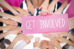 A pink card that says Get Involved being held by a circle of hands, slightly blurry in the background.
