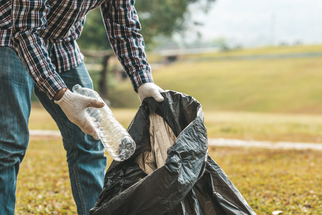 A man is picking up trash in a park, not throwing trash in the trash can ruin the beauty of the garden area and also cause global warming and harm animals. Concept of cleanliness in public areas.